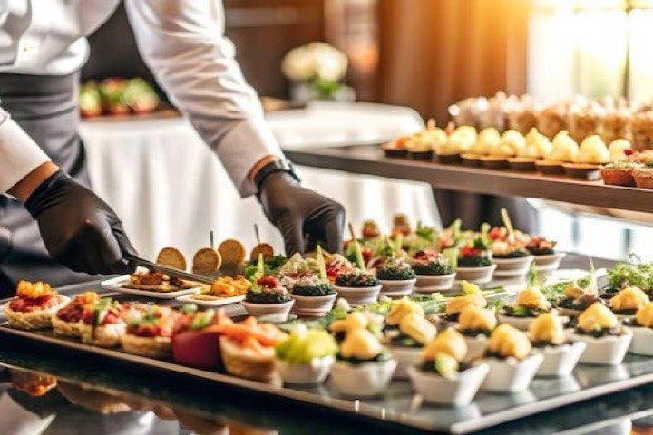 A chef in gloves plating rows of canapes onto a mirrored buffet tray