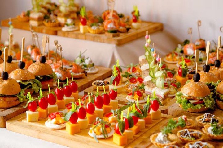 A spread of canapes, sliders and skewers laid out on wooden serving boards